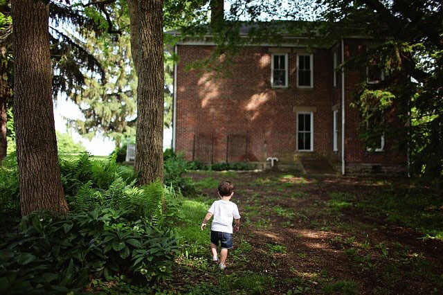 Young boy walking through spring trees behind brick house.